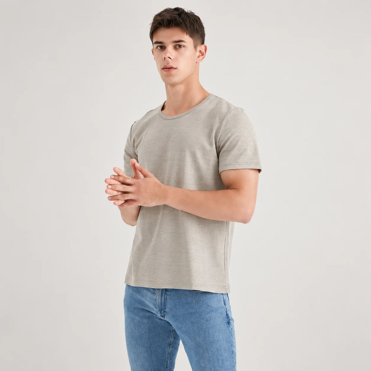 Silver-grey AJ512 round-neck T-shirt worn with blue jeans, with the model standing and hands together.