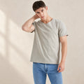 Silver-grey AJ512 T-shirt styled with blue jeans against a warm neutral studio background.