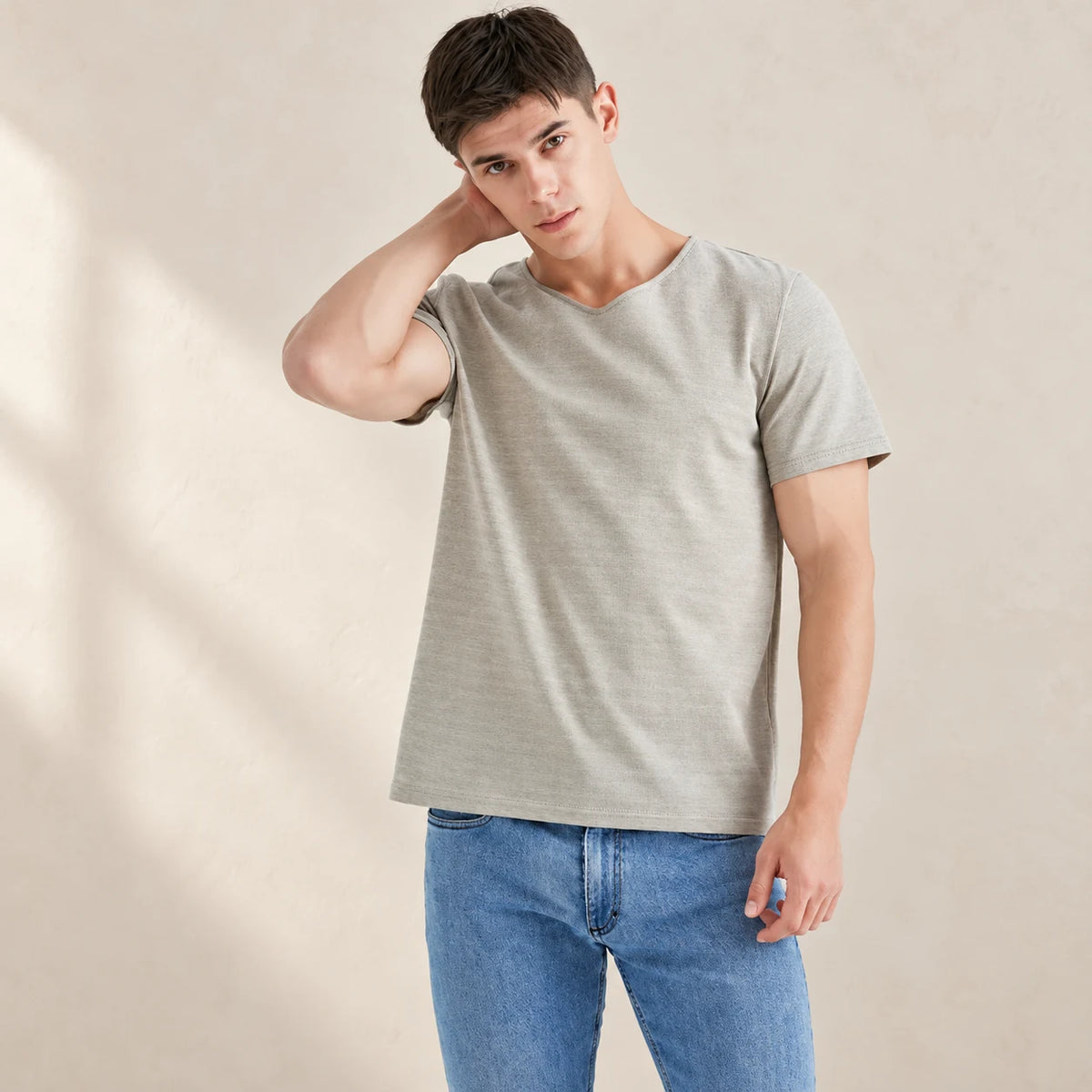 Silver-grey AJ512 T-shirt styled with blue jeans against a warm neutral studio background.